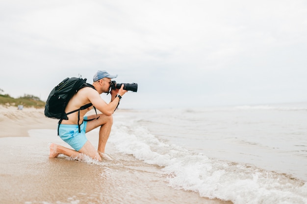Uomo con la macchina fotografica della foto che prende immagine del mare. Ubicazione del fotografo dell'uomo sulla spiaggia e scattare foto della natura