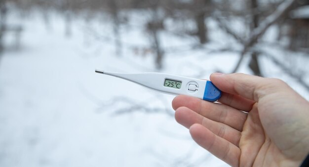 Uomo con la mano che mostra il termometro in inverno