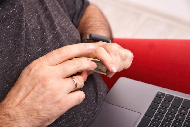 Uomo con laptop in grembo e denaro in mano concetto di business online primo piano