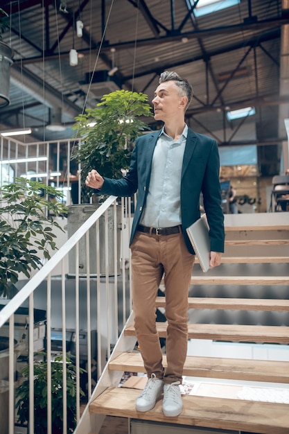 Uomo con laptop in piedi sulle scale in casa