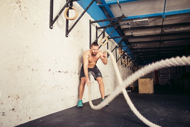 Uomo con le corde di battaglia che si esercitano nella palestra di forma fisica