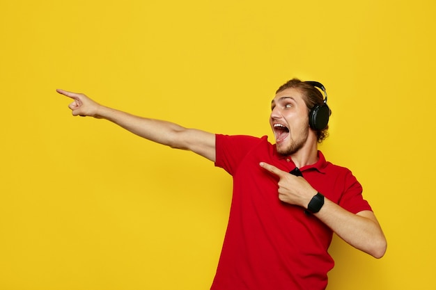 Uomo con le cuffie e la maglietta polo rossa che punta lontano con entrambe le mani