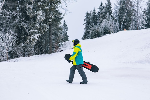 Uomo con lo snowboard che cammina per le attività invernali di collina innevata