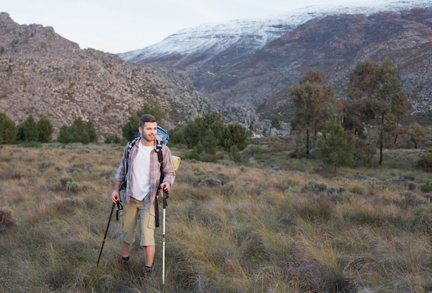 Uomo con lo zaino e bastoncini da trekking a piedi sul paesaggio