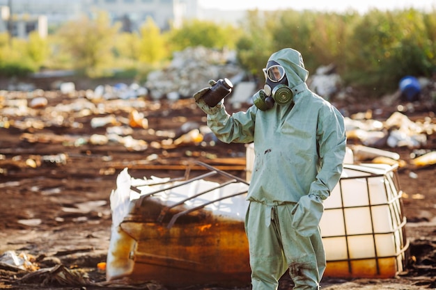 Uomo con maschera antigas e abiti militari verdi esplora i barili dopo il disastro chimico