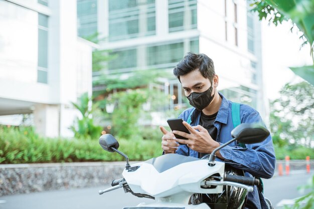 Uomo con maschera che utilizza un cellulare su una moto sullo sfondo della strada della città