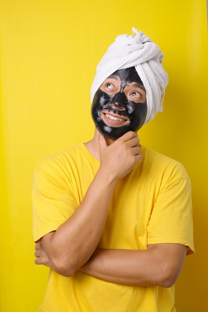 Uomo con maschera cosmetica sul viso su sfondo giallo Concetto di bellezza e cura della pelle