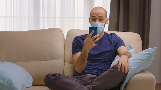Uomo con maschera di protezione durante l'isolamento del coronavirus durante una videochiamata con la sua famiglia.