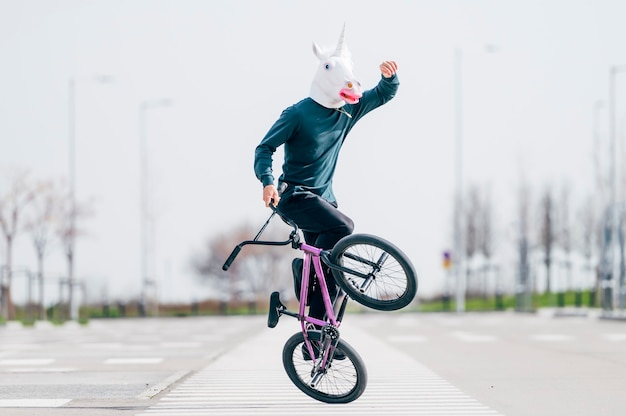 Uomo con maschera di unicorno in sella a una bicicletta