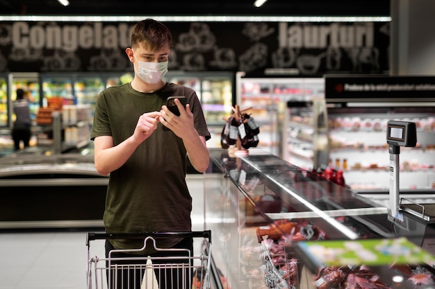 Uomo con maschera medica che utilizza smartphone al supermercato