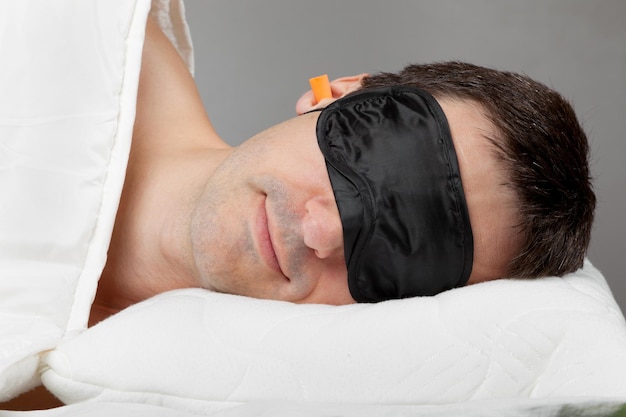 Uomo con maschera per dormire e tappi per le orecchie sdraiato a letto