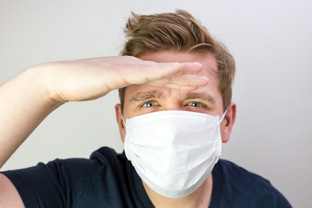 Uomo con maschera per proteggerlo dal virus. Il concetto di epidemia di coronavirus. Medico stanco con maschera bianca medica. Non vedo, dove sei. Uomo che guarda lontano