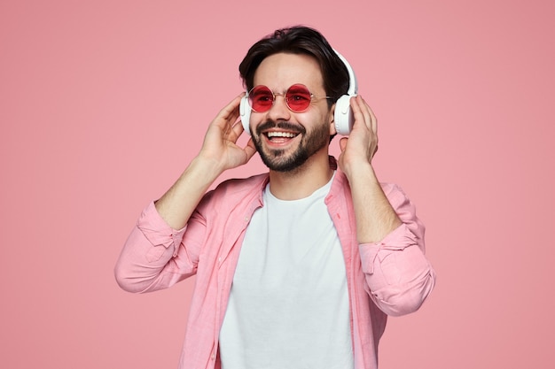 Uomo con occhiali da sole che ascolta la musica in cuffia sopra la parete rosa