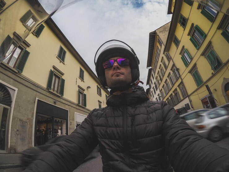 Foto uomo con occhiali da sole e casco in mezzo agli edifici della città