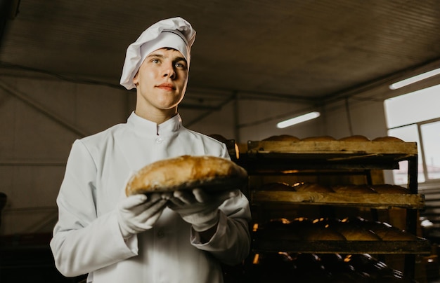 Uomo con pane fresco nelle sue mani panettiere in grembiule e camicia che dà pane caldo su sfondo nero