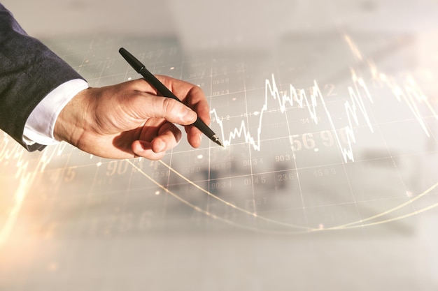 Uomo con penna che lavora con un grafico finanziario virtuale astratto sullo sfondo sfocato dell'ufficio forex e concetto di investimento Multiesposizione