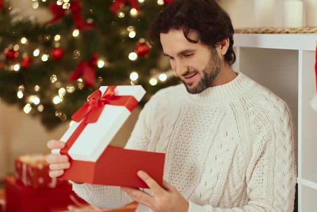 Uomo con regalo nella confezione regalo vicino all'albero di Natale a casa