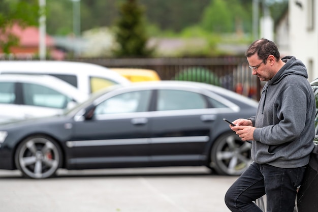 Uomo con smartphone in piedi accanto all'auto che utilizza l'app mobile per pagare il blocco dell'auto o Internet