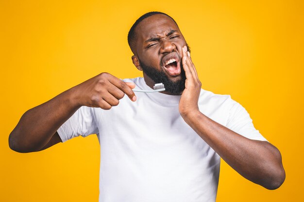 Uomo con spazzolino da denti e mal di denti. Immagine di giovane uomo africano senza camicia che tiene uno spazzolino da denti con dentifricio e mela,