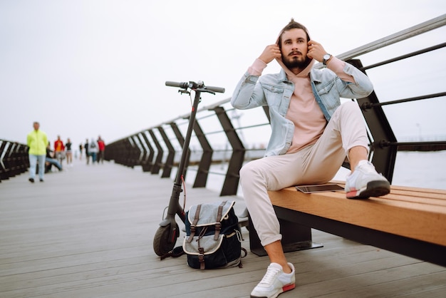 Uomo con tablet in sella a uno scooter elettrico sul molo vicino al mare Libero professionista Trasporto ecologico in città