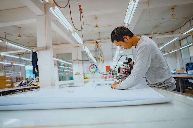 Uomo con taglierina e dispositivi di protezione individuale sul posto di lavoro industriale di abbigliamento Tessuto