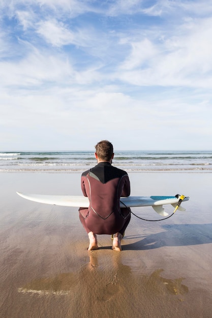 Uomo con tavola da surf accovacciato sulla spiaggia