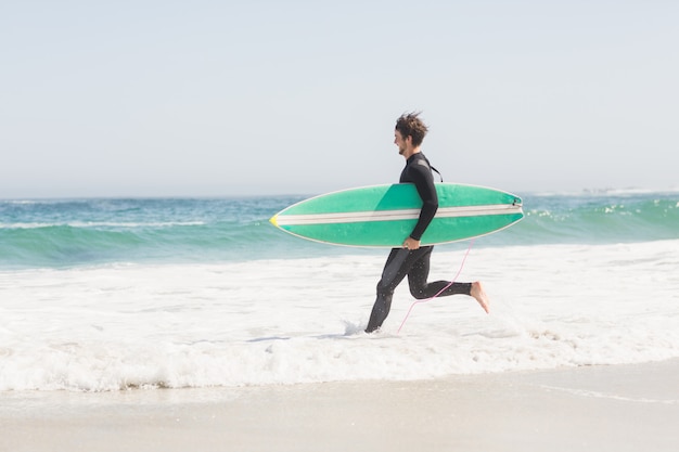 Uomo con tavola da surf che corre verso il mare