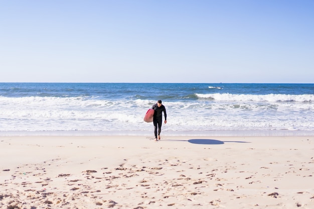 uomo con tavola da surf sulla riva dell&#39;oceano. Surfer in una muta