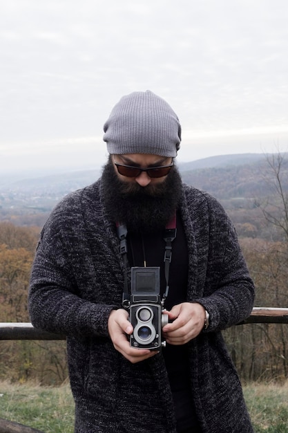 Uomo con un cappello a maglia che tiene la telecamera in piedi contro il cielo