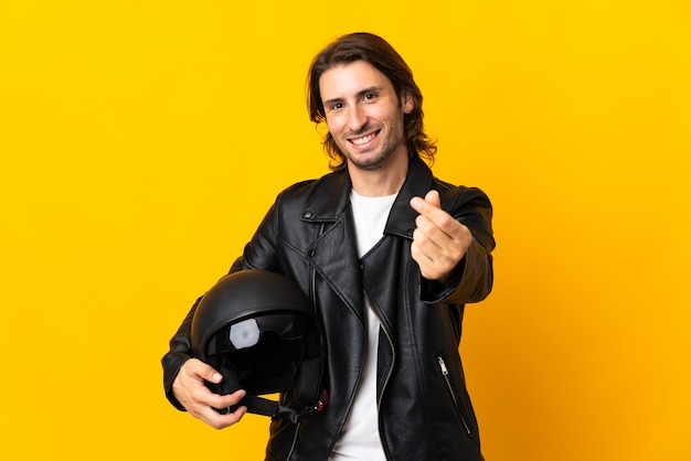 Uomo con un casco da motociclista isolato sulla parete gialla che fa gesto di soldi