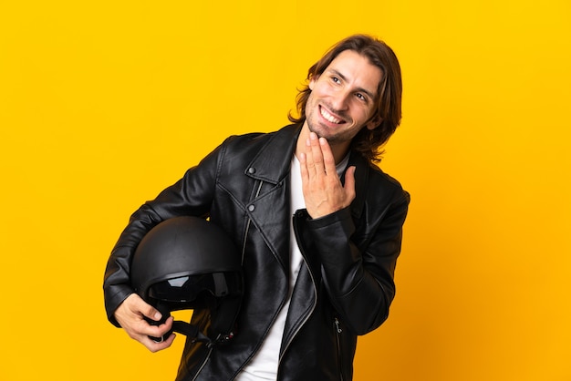 Uomo con un casco da motociclista isolato sulla parete gialla che osserva in su mentre sorride