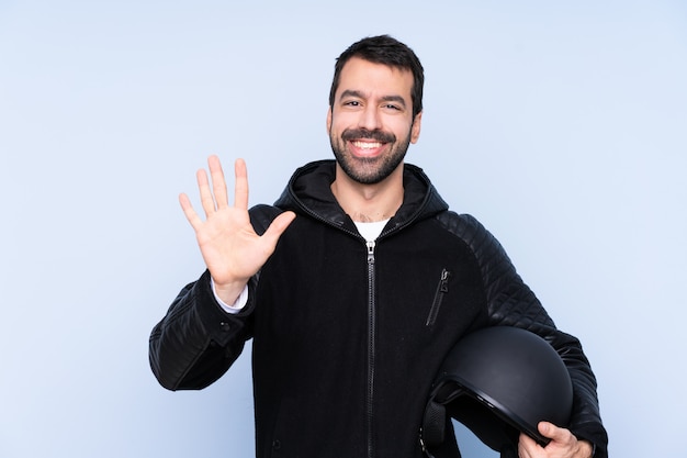 Uomo con un casco del motociclo sopra la parete isolata che conta cinque con le dita