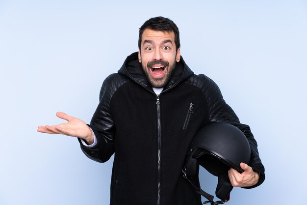 Uomo con un casco del motociclo sopra la parete isolata con espressione facciale colpita