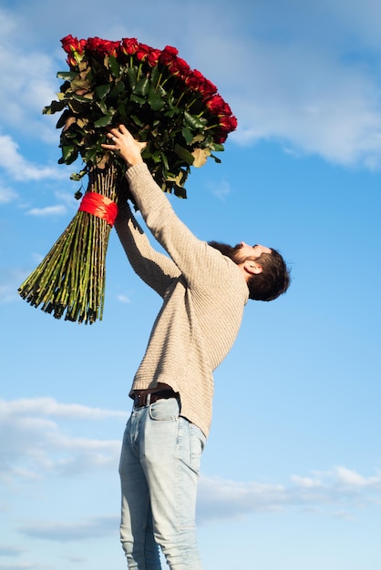 Uomo con un grande mazzo di rose. Festeggia San Valentino e regali romantici. Bel ragazzo tiene in mano un mazzo di grandi rose rosse. Bell'uomo che dà fiori al suo amante il giorno di San Valentino.