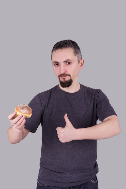 Uomo con una barba che mangia un panino sopra fondo grigio