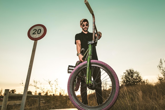 Uomo con una bicicletta sul campo contro il cielo durante il tramonto