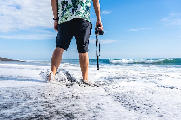 Uomo con una macchina fotografica che cammina nell'acqua del mare