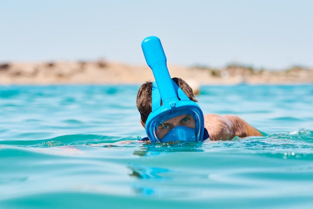 Uomo con una maschera a pieno facciale della presa d'aria che si tuffa mare blu. Vacanze estive