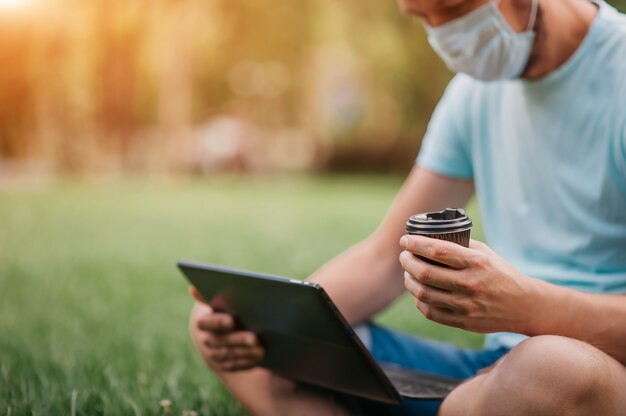 Uomo con una maschera protettiva utilizzando un computer portatile in natura