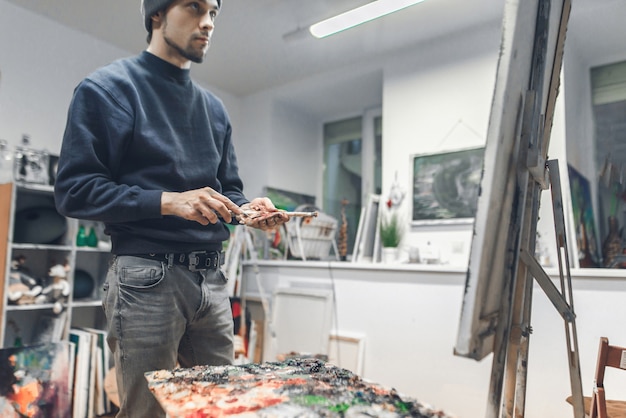 Uomo concentrato in piedi in uno studio vicino alla tela e dipinge un quadro