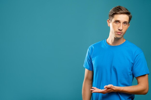 Uomo confuso Gesto di benvenuto Banner informativo Giovane ragazzo che tiene la mano che punta lo spazio della copia guardando la fotocamera isolata su sfondo blu Pubblicità