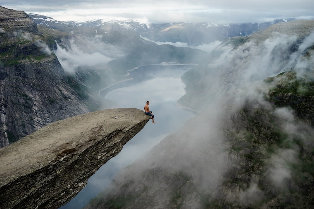 Uomo coraggioso seduto sul bordo di Trolltunga