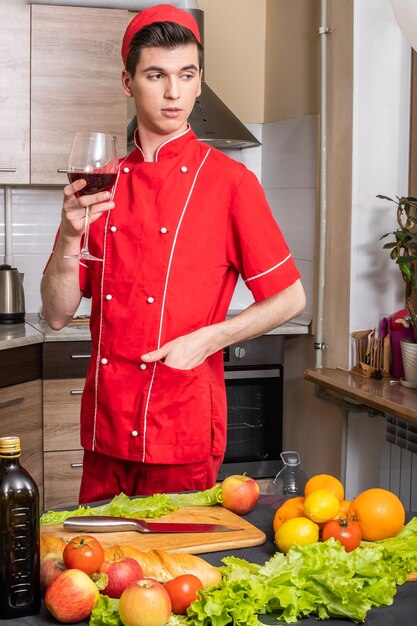 Uomo Cuoco in divisa rossa che assaggia il vino in cucina