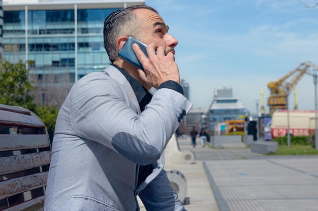 uomo d'affari adulto seduto all'aperto a parlare al telefono guardando il cielo e riflessivo