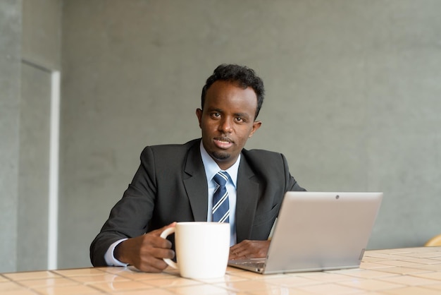 Uomo d'affari africano che indossa giacca e cravatta nella caffetteria durante l'utilizzo di un computer portatile