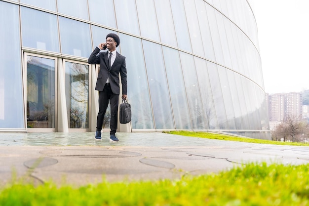 Uomo d'affari africano che parla con il cellulare che tiene la borsa del computer all'aperto