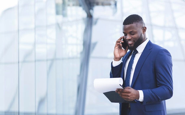 Uomo d'affari africano che parla sul cellulare che negozia l'affare in piedi all'aperto