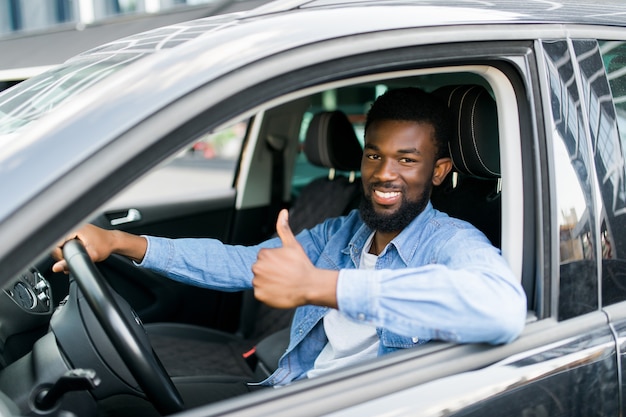 Uomo d'affari africano felice che dà pollice in su all'interno della nuova automobile