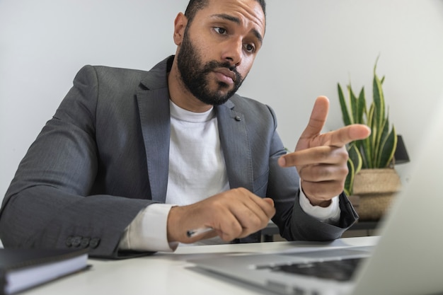 Uomo d'affari afroamericano che parla con un collega in videochiamata puntando il dito sullo schermo del laptop