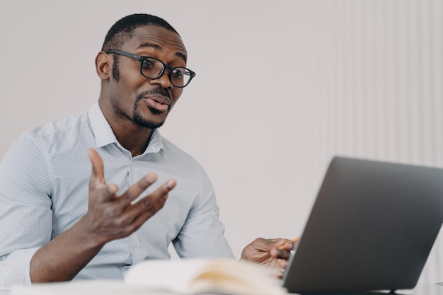 Uomo d'affari afroamericano con gli occhiali che discute progetto di lavoro tramite videochiamata al computer portatile